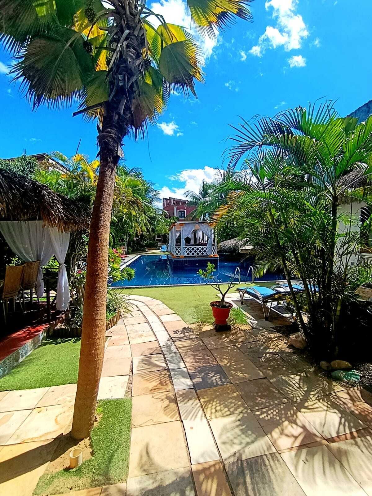 A pool area with a boat, palm trees, and a thatched-roof structure.