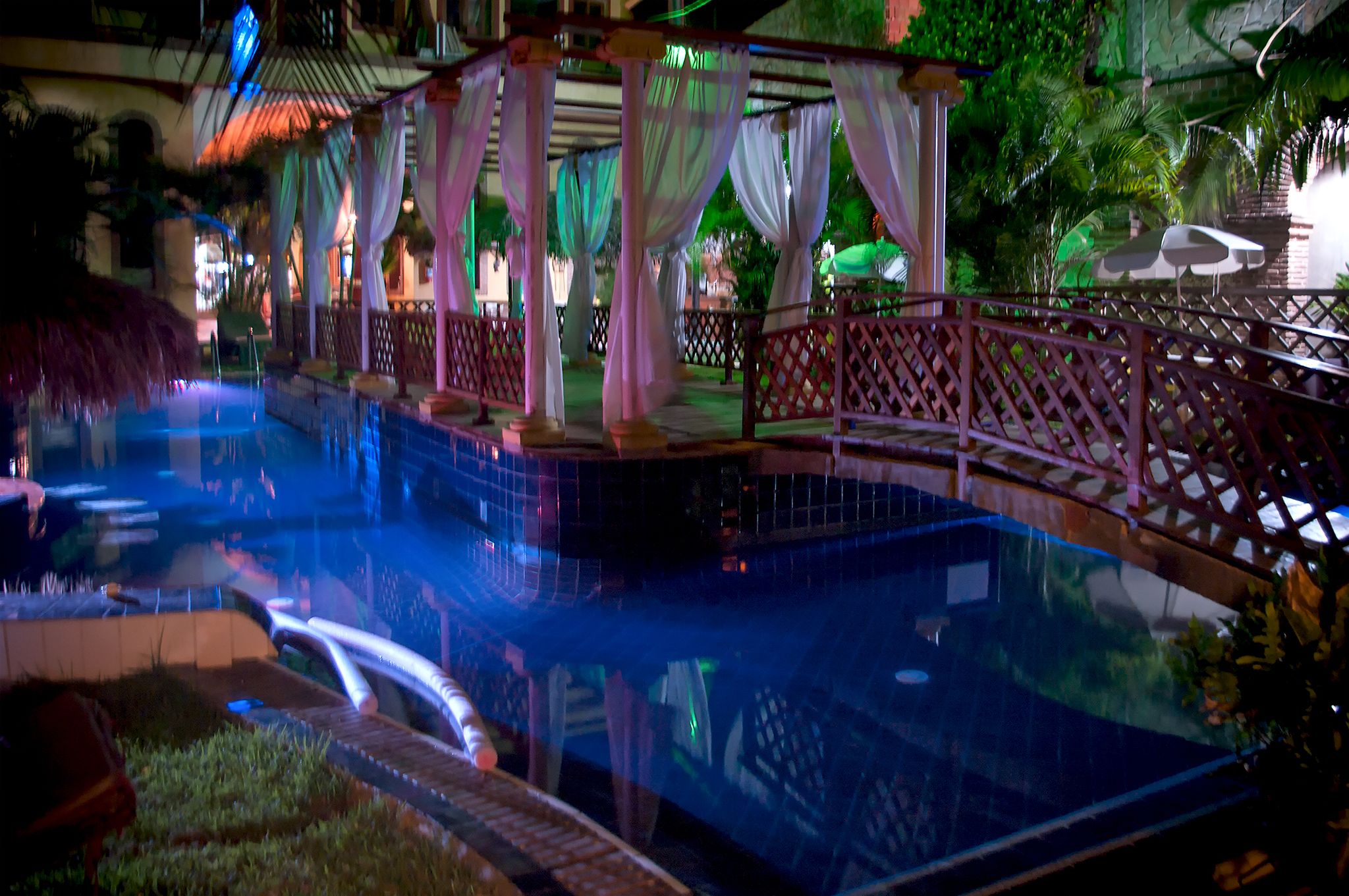 Uma área de piscina com uma ponte, cercada por uma grade e decorada com cortinas brancas.