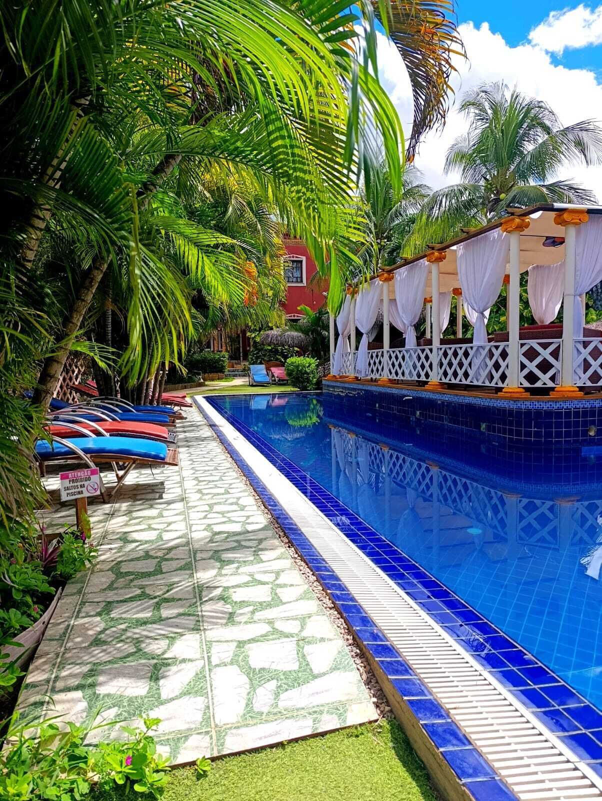 A poolside area with lounge chairs, a covered seating area, and a tiled walkway.