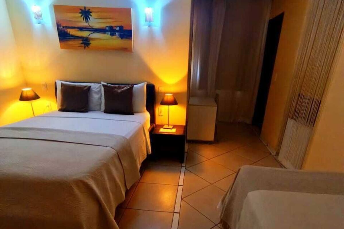 A hotel room with two beds, a painting on the wall, and two wall-mounted lamps.
