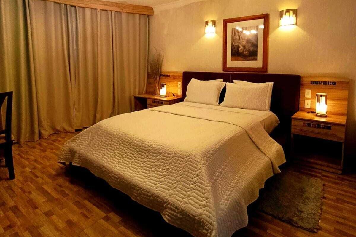 A bedroom with a large bed, wooden flooring, a ceiling light fixture, and two bedside lamps.