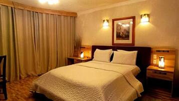 A bedroom with a large bed, wooden flooring, a ceiling light fixture, and two bedside lamps.
