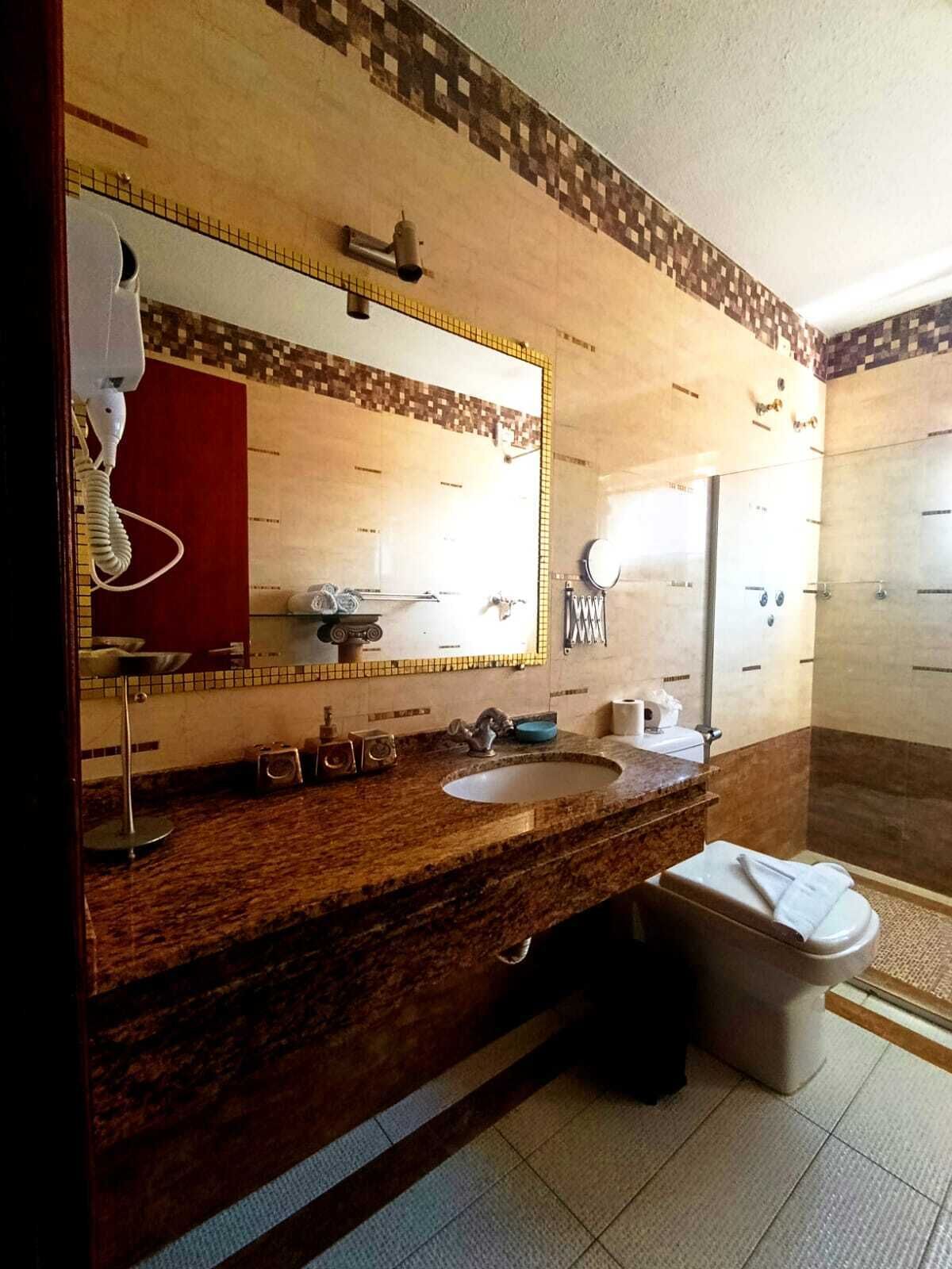 Une salle de bain avec un meuble-lavabo en marbre, un grand miroir, un lavabo, des toilettes et un espace douche.