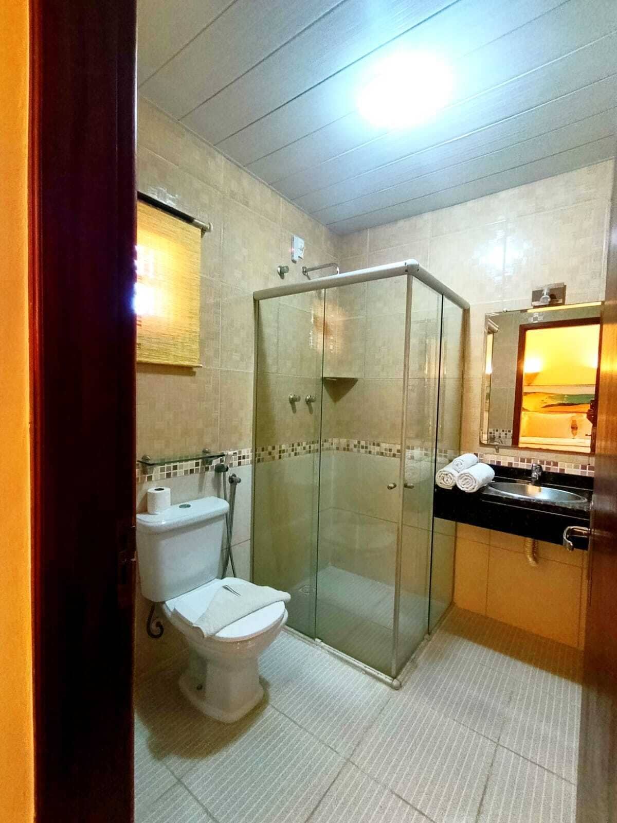 Casa de banho com cabine de chuveiro em vidro, sanita, lavatório e espelho.