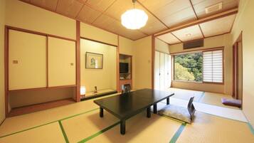 A traditional Japanese room with tatami flooring, a low table, sliding doors, and a view of greenery outside.