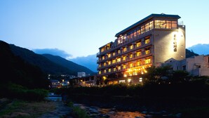 Et hotel med flere etager foran en flod, omgivet af bjerge.