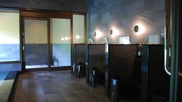 A modern restroom with glass partitions, a tiled floor, and wall-mounted lights.