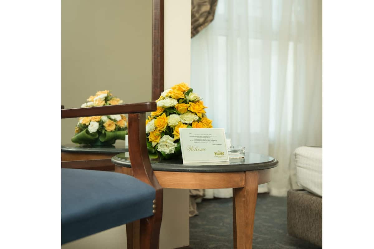 A hotel room with a wooden chair, a small round table with a welcome card, and a bouquet of yellow and white flowers.