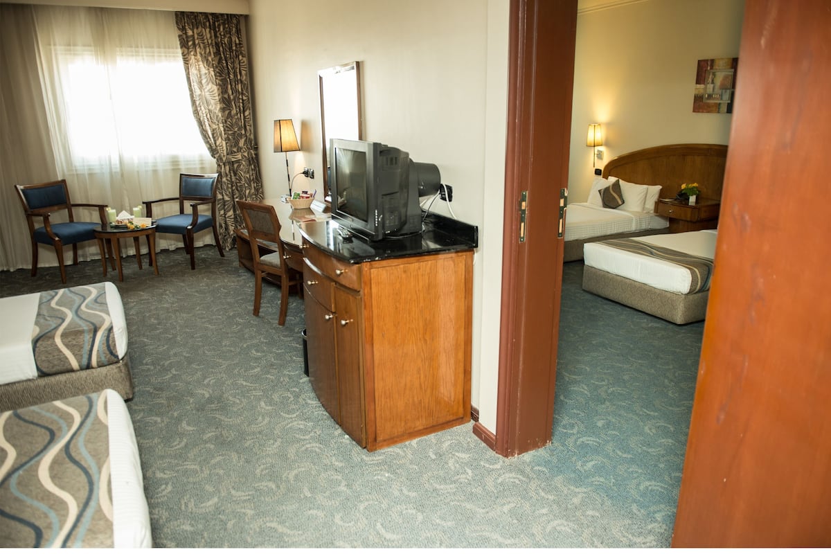 A hotel room with a desk, television, two chairs, a bed, and a sofa.