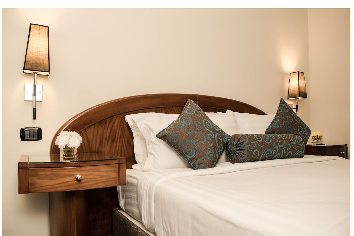 A neatly made bed with patterned pillows, a bedside table with a lamp, and a small vase with flowers.