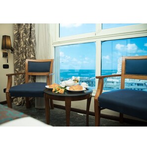 A hotel room with two wooden chairs, a small table with plates of food, a teapot, and a cup. A window offers a view of the cityscape. - Cherry Maryski Hotel (Alexandria)