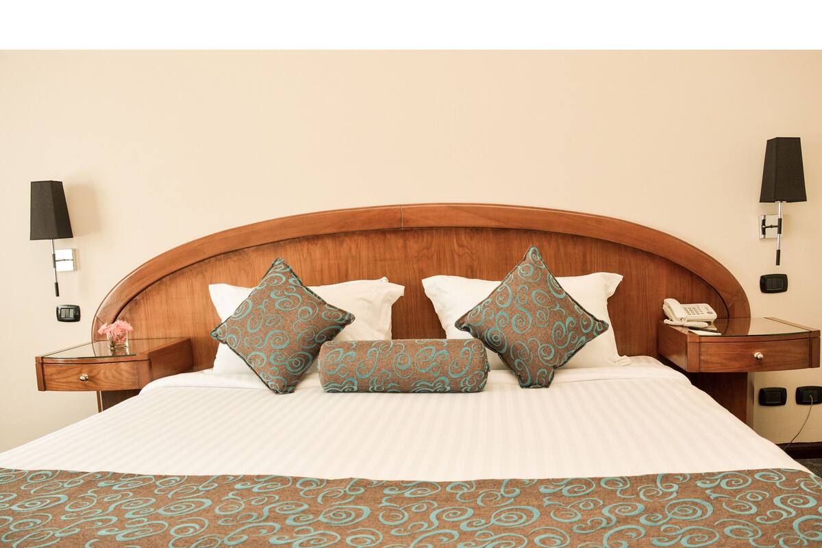 A neatly made bed with a patterned bedspread, a wooden headboard, and decorative pillows. There are bedside tables with lamps and a telephone on one side.