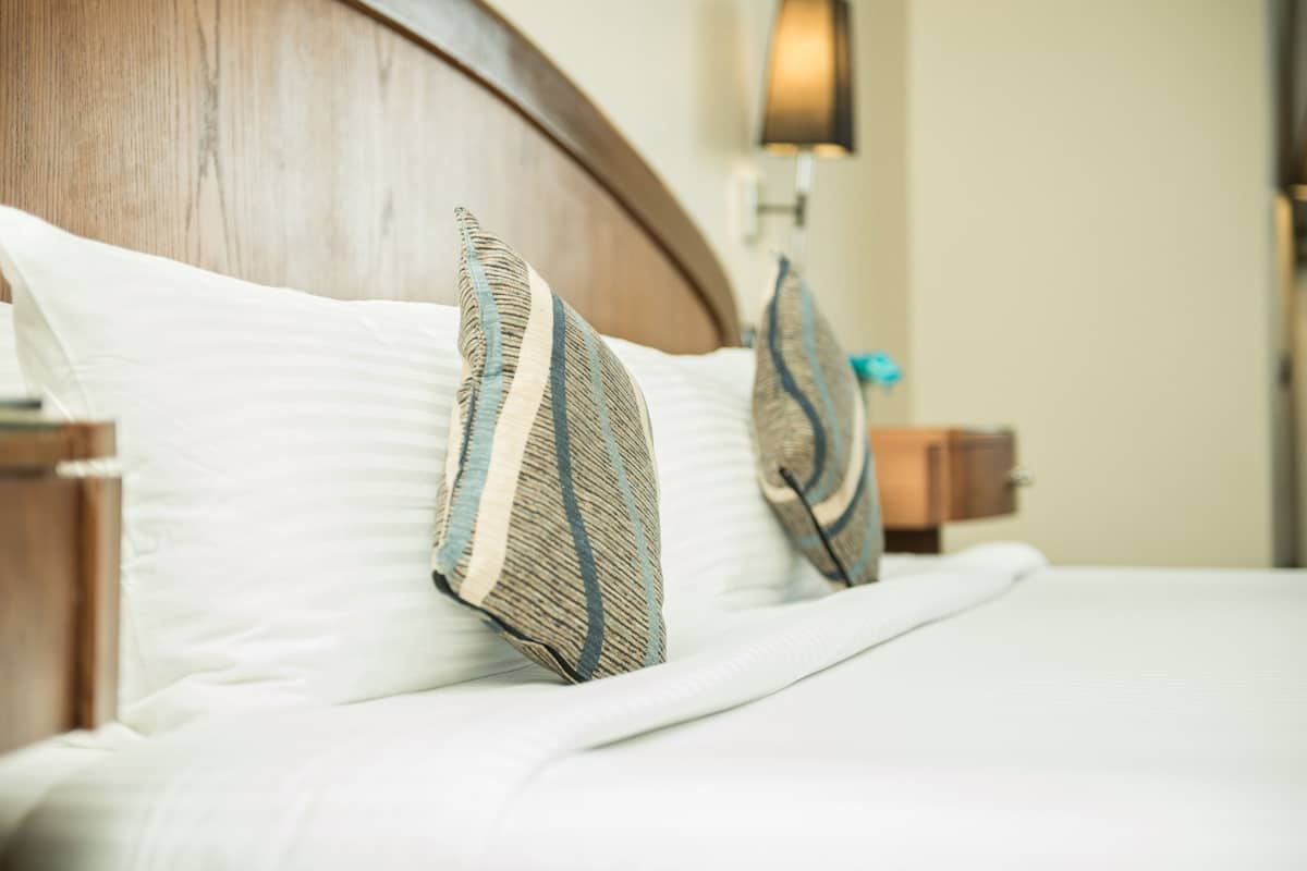 A neatly made bed with white linens and two decorative pillows with blue and beige stripes.