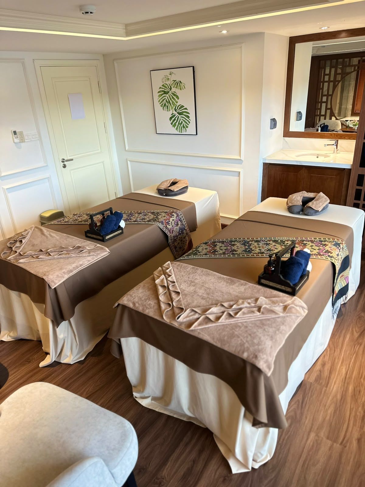 Une chambre d’hôtel avec deux lits, une petite table, un banc, un miroir et une plante accrochée au mur.
