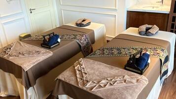 Une chambre d’hôtel avec deux lits, une petite table, un banc, un miroir et une plante accrochée au mur.