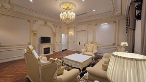 Une chambre luxueuse, agrémentée de motifs dorés raffinés, d’un lustre, d’une télévision et de fauteuils confortables.