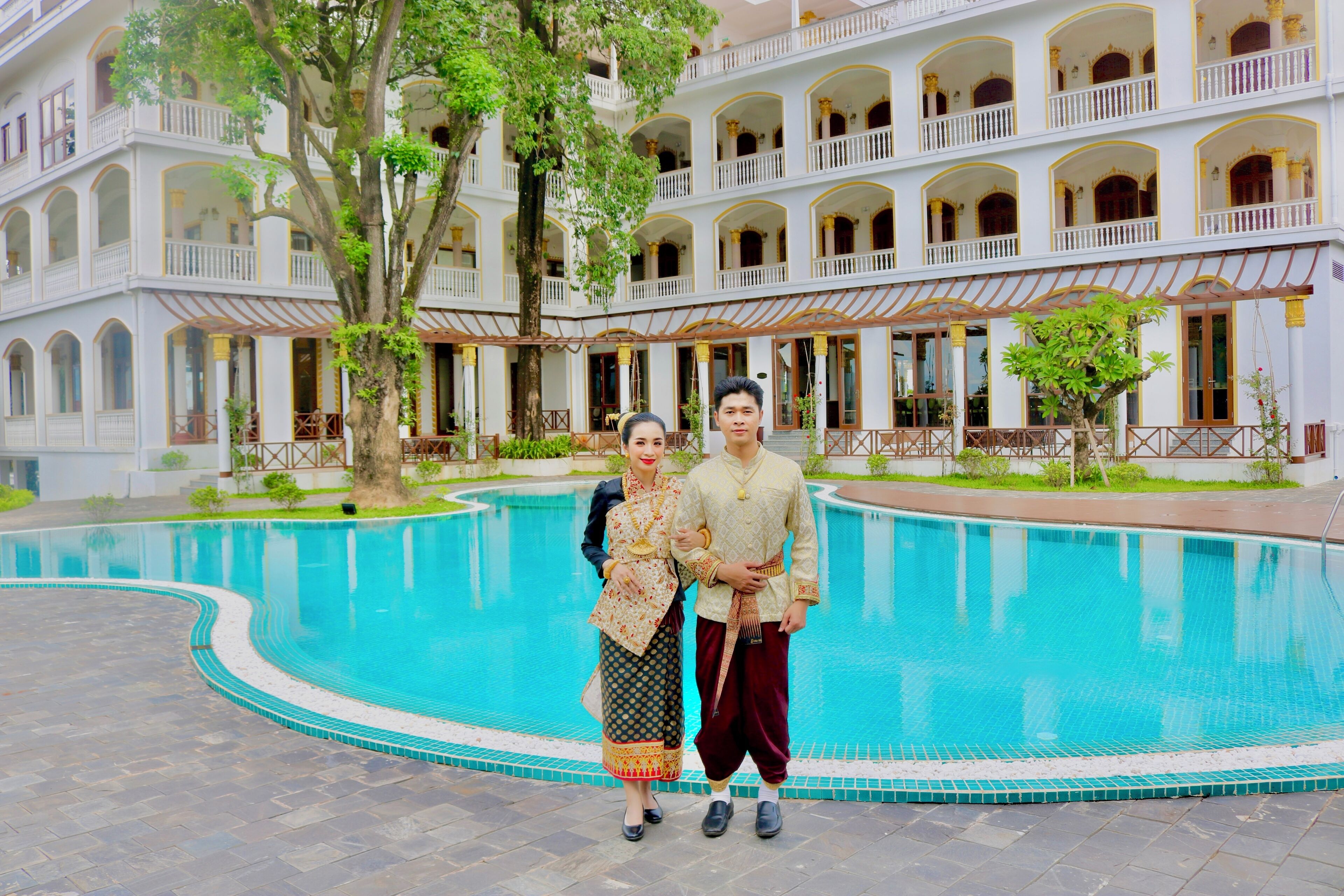 Un couple se tient près d’une piscine, avec un immeuble à plusieurs étages en arrière-plan.