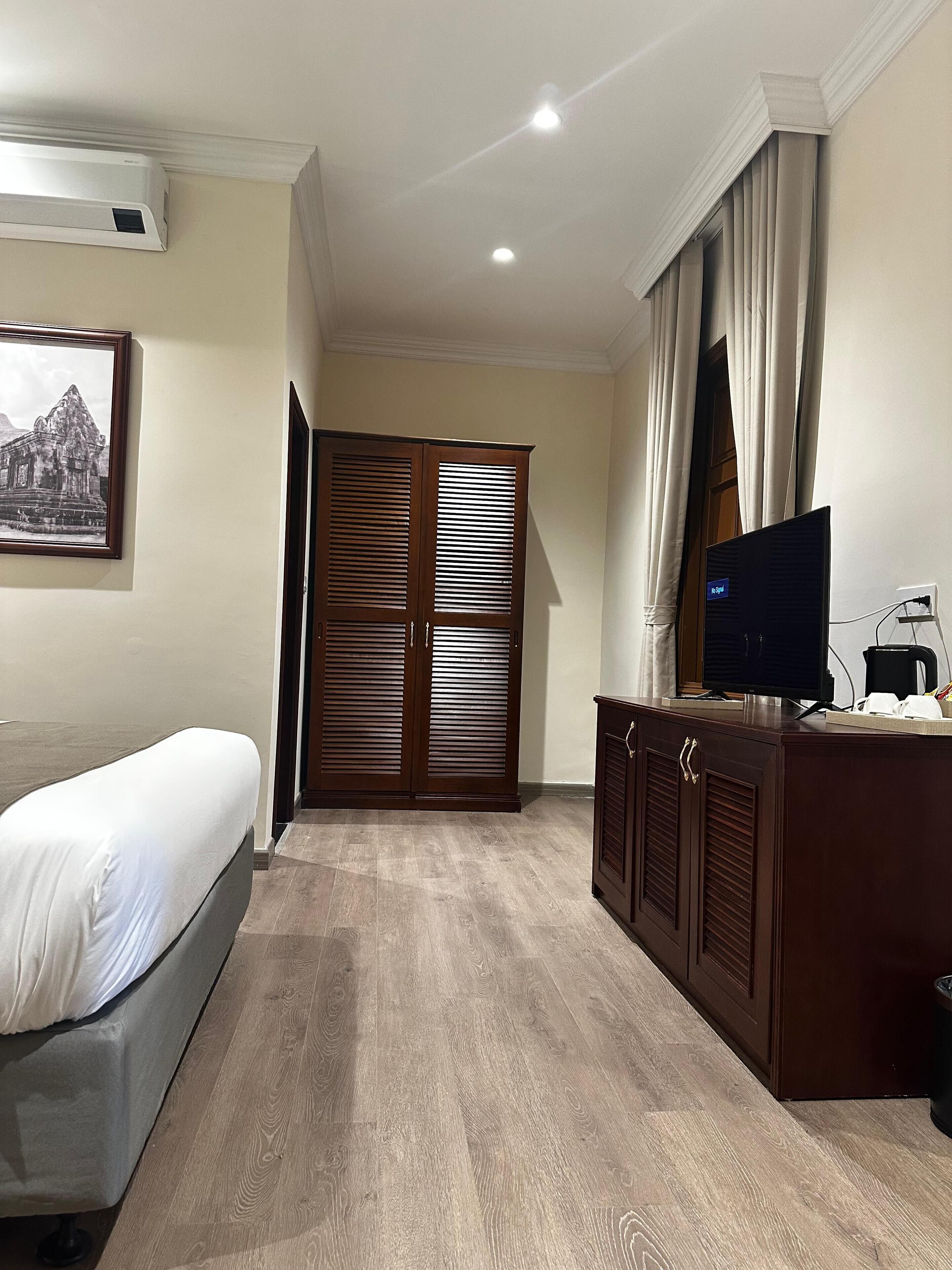 A hotel room with a bed, a TV, a coffee maker, and a wardrobe.