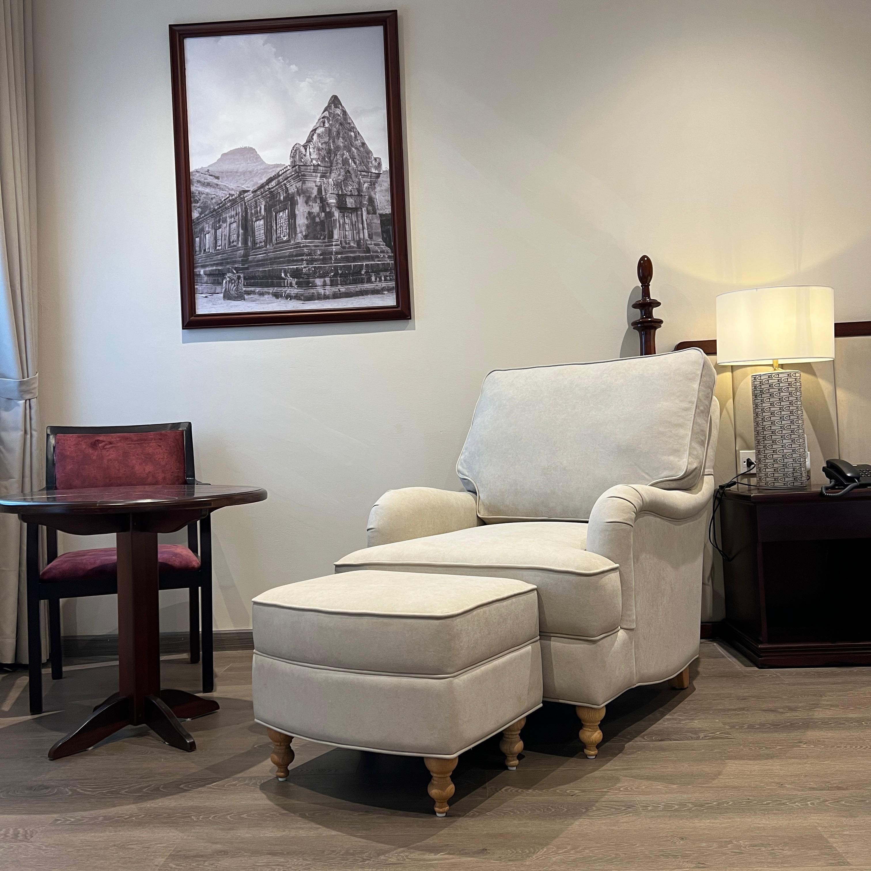 A room with a large armchair, a small table, a lamp, and a framed picture on the wall.