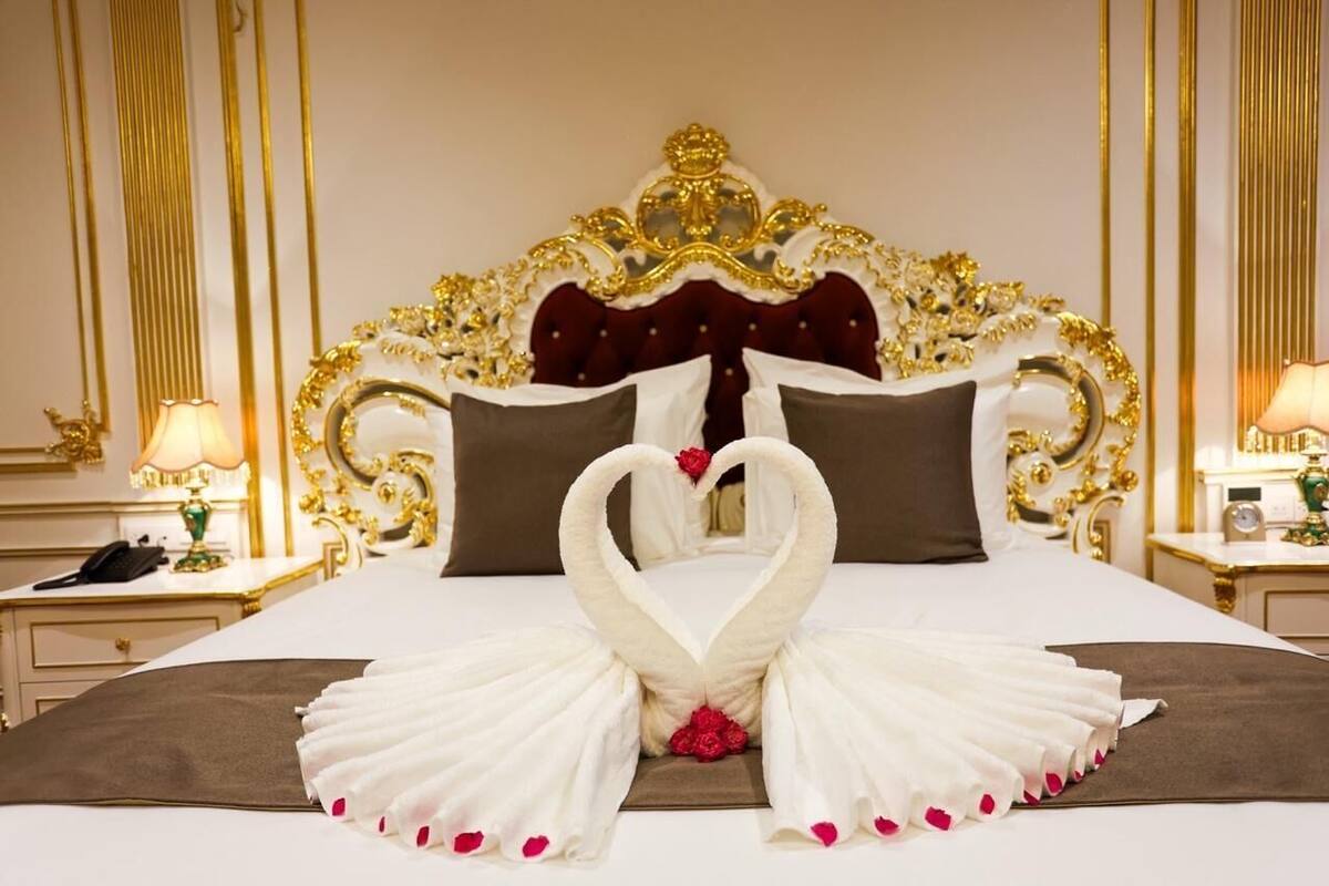 A luxurious hotel room with an ornate bed, a heart-shaped towel arrangement, and a classic decor style.