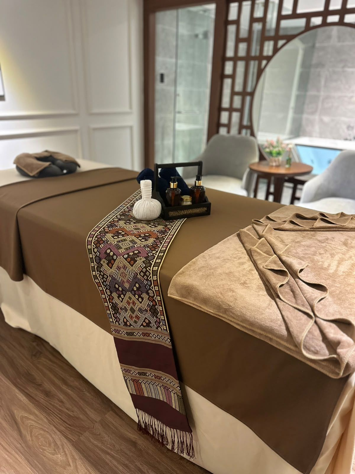 A neatly made bed with a patterned runner, a pair of slippers, and a small toiletry set on the side.