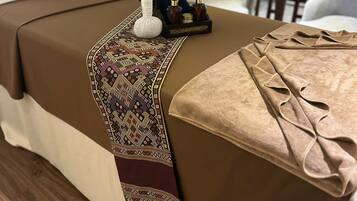A neatly made bed with a patterned runner, a pair of slippers, and a small toiletry set on the side.