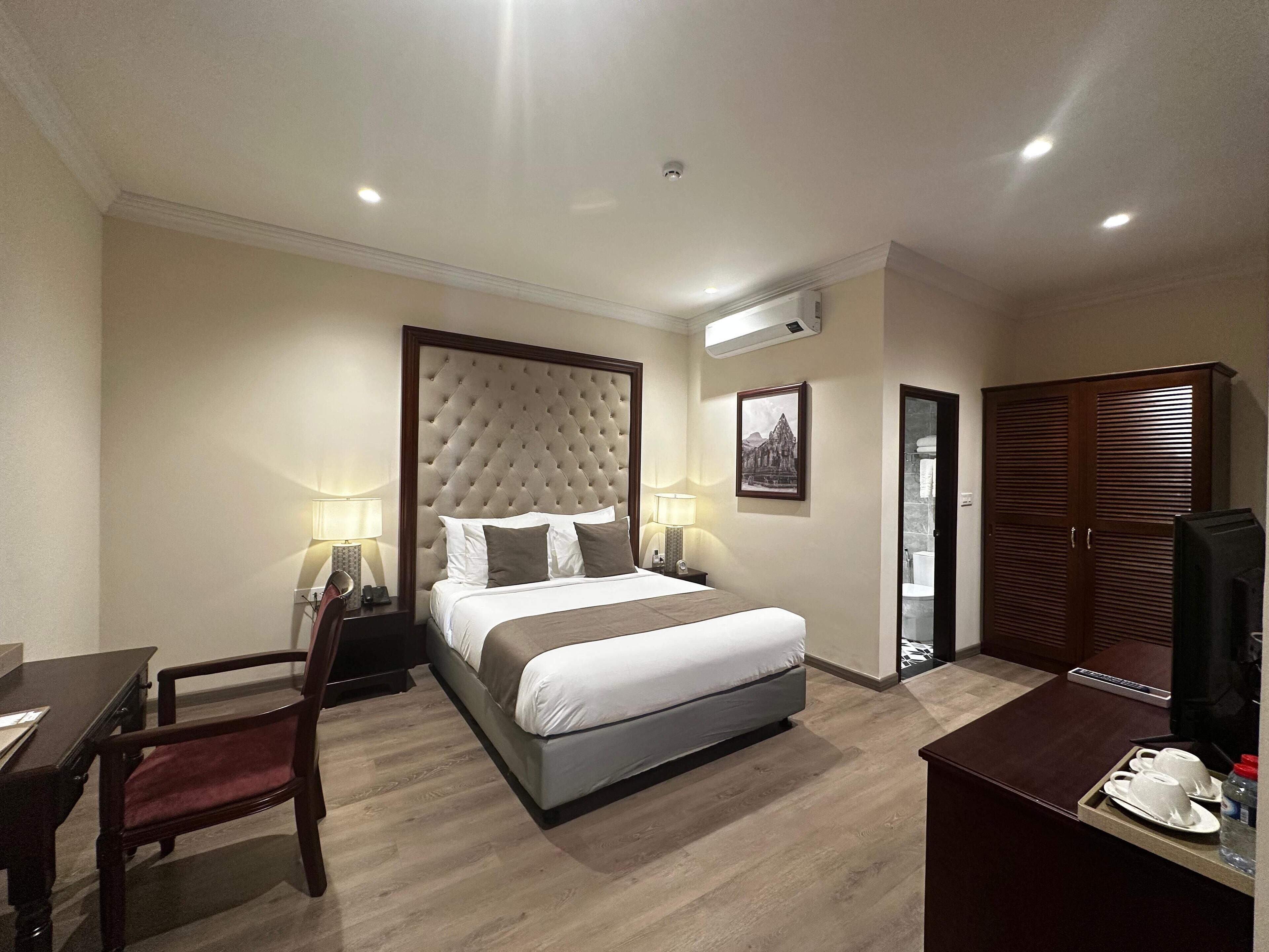 A hotel room with a large bed, a desk, a chair, a wardrobe, and a television.