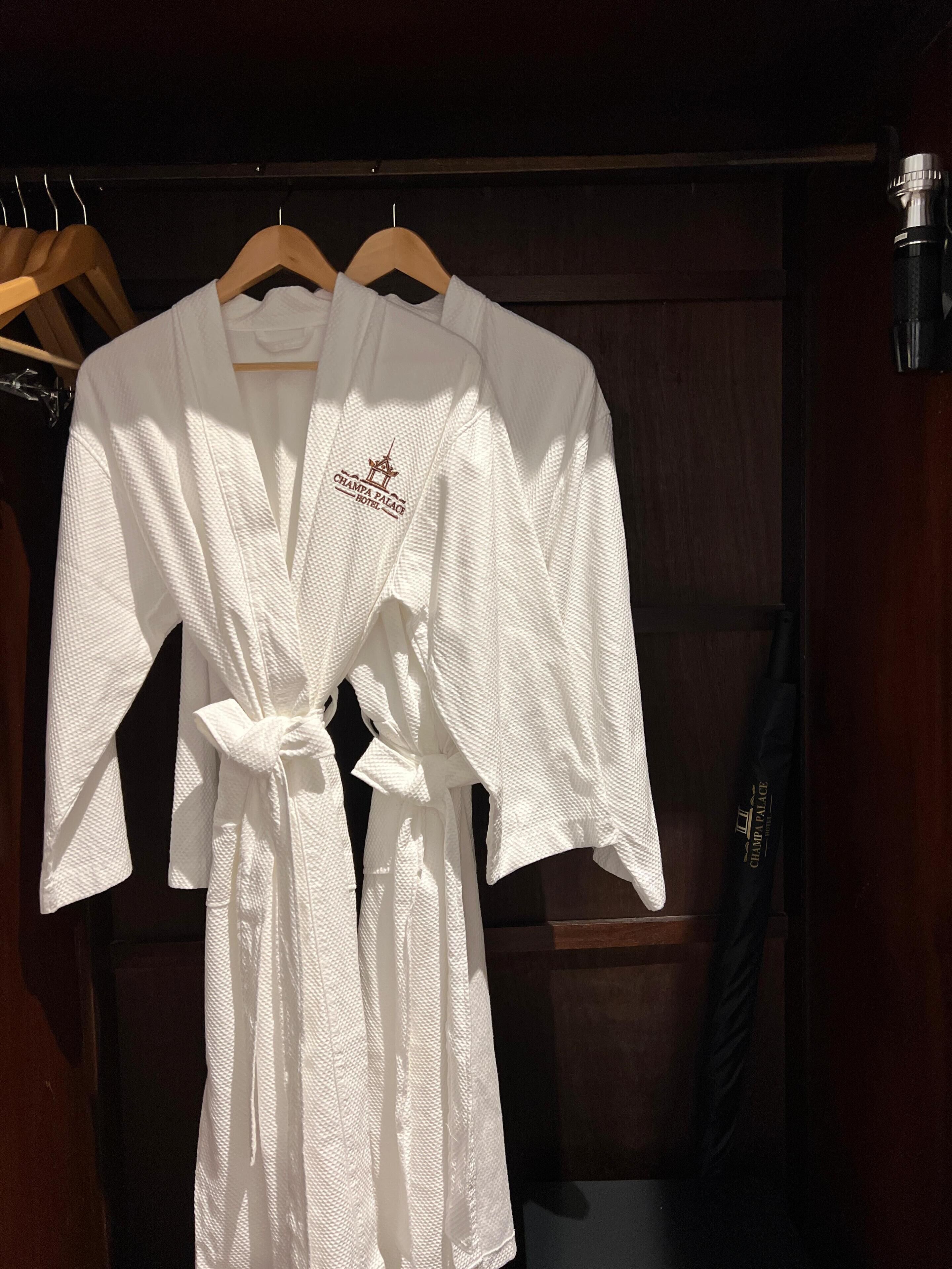 Two white robes hanging on wooden hangers in a wooden closet.