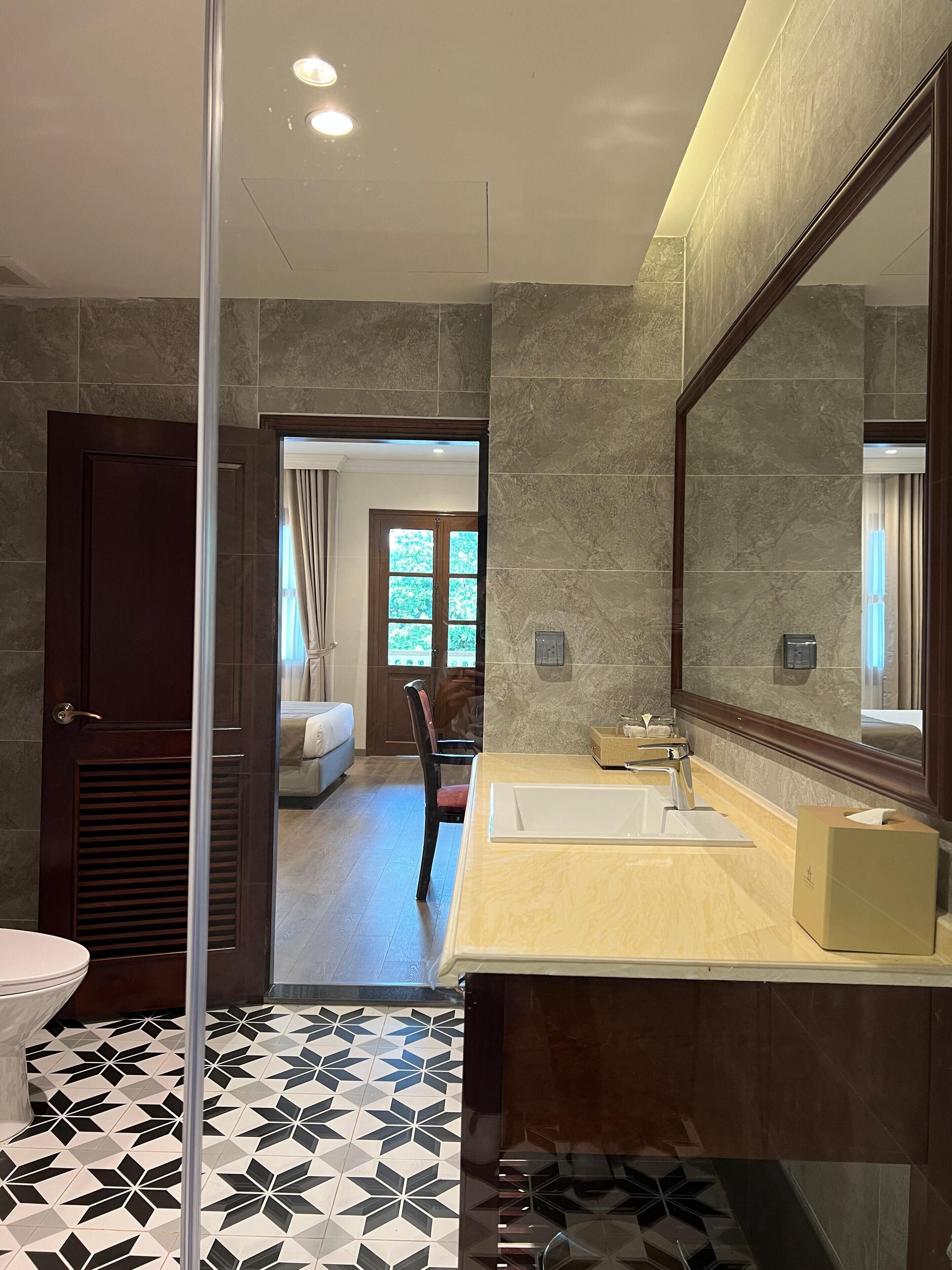 A modern bathroom with a large mirror, a sink, and a toilet. The floor has a geometric tile pattern.