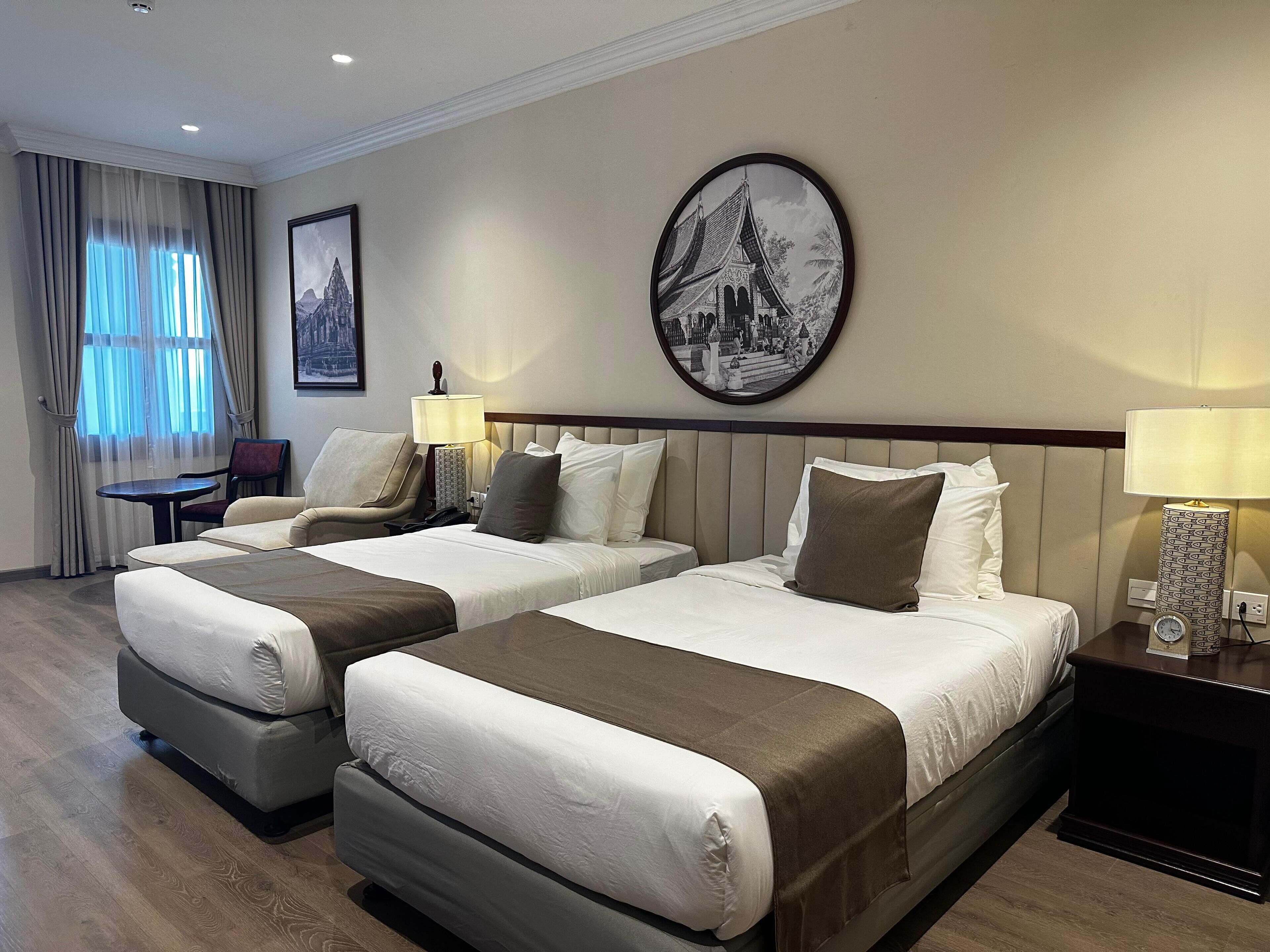 Habitación de hotel con dos camas, una silla, una mesa y un reloj de pared.