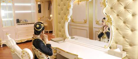 A luxurious room with a tufted wall, a large ornate mirror, and a white vanity with gold accents.