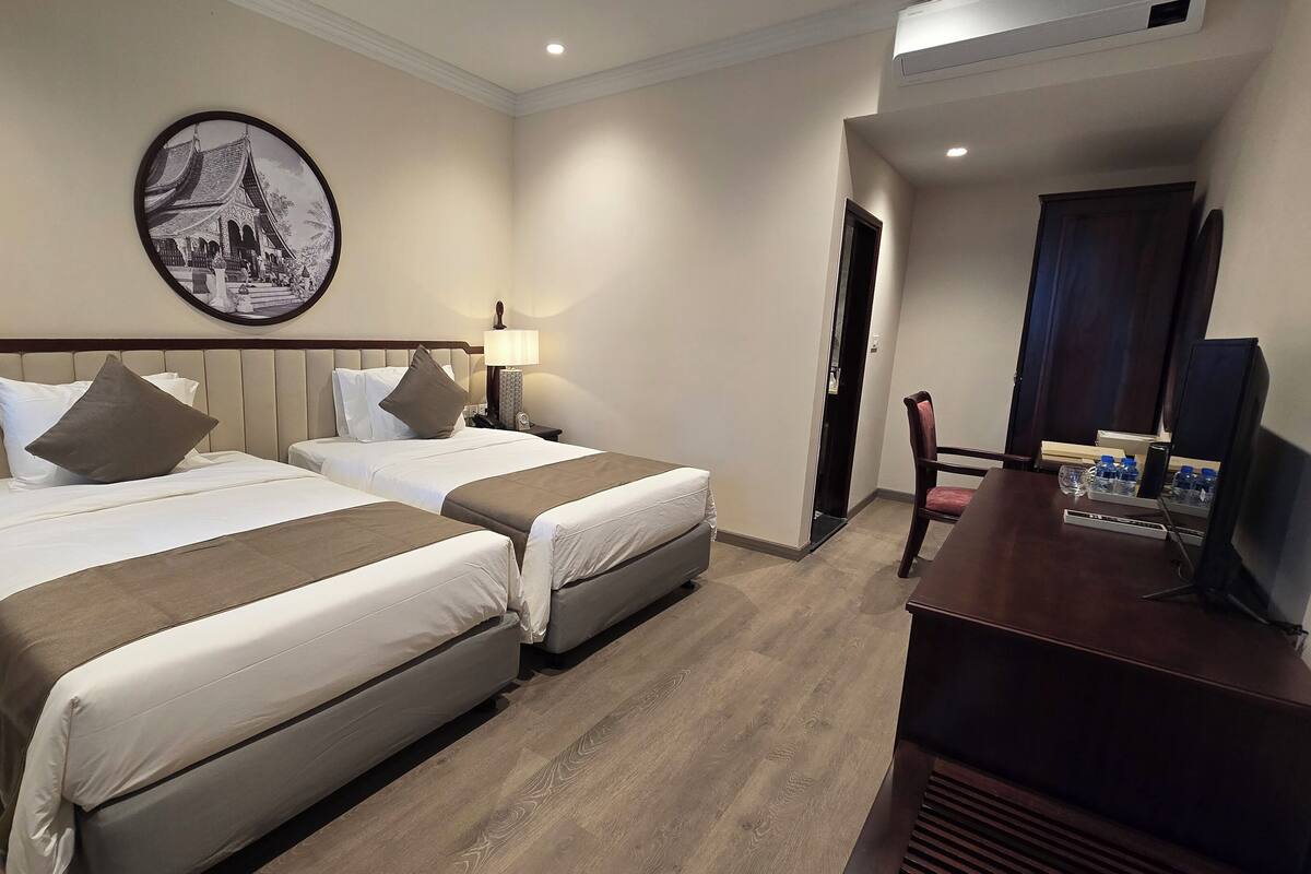 A hotel room with two beds, a television, a desk with a chair, and a wall-mounted picture.