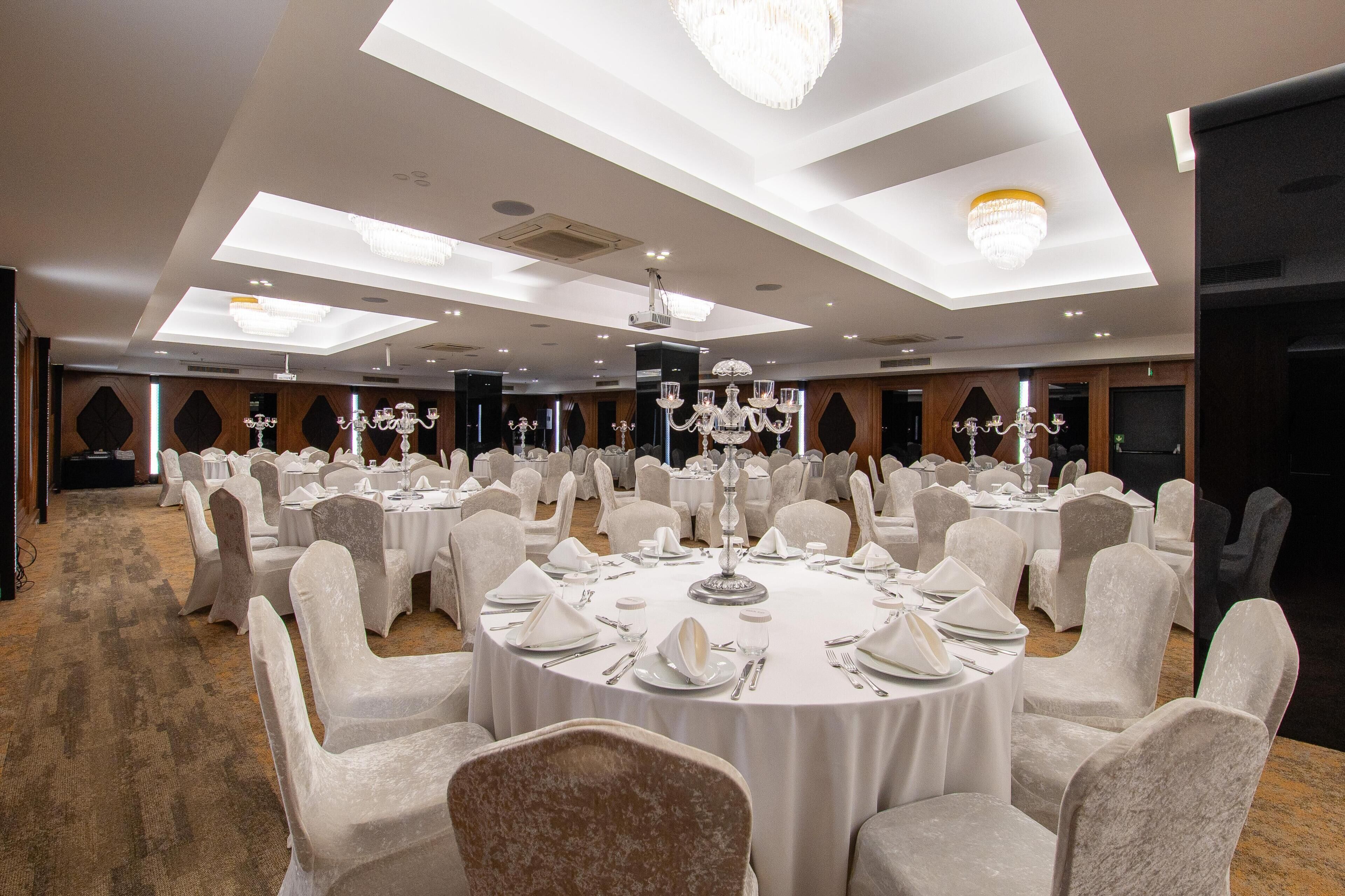 Un salón de banquetes con mesas redondas, manteles blancos y sillas cubiertas con tela blanca.