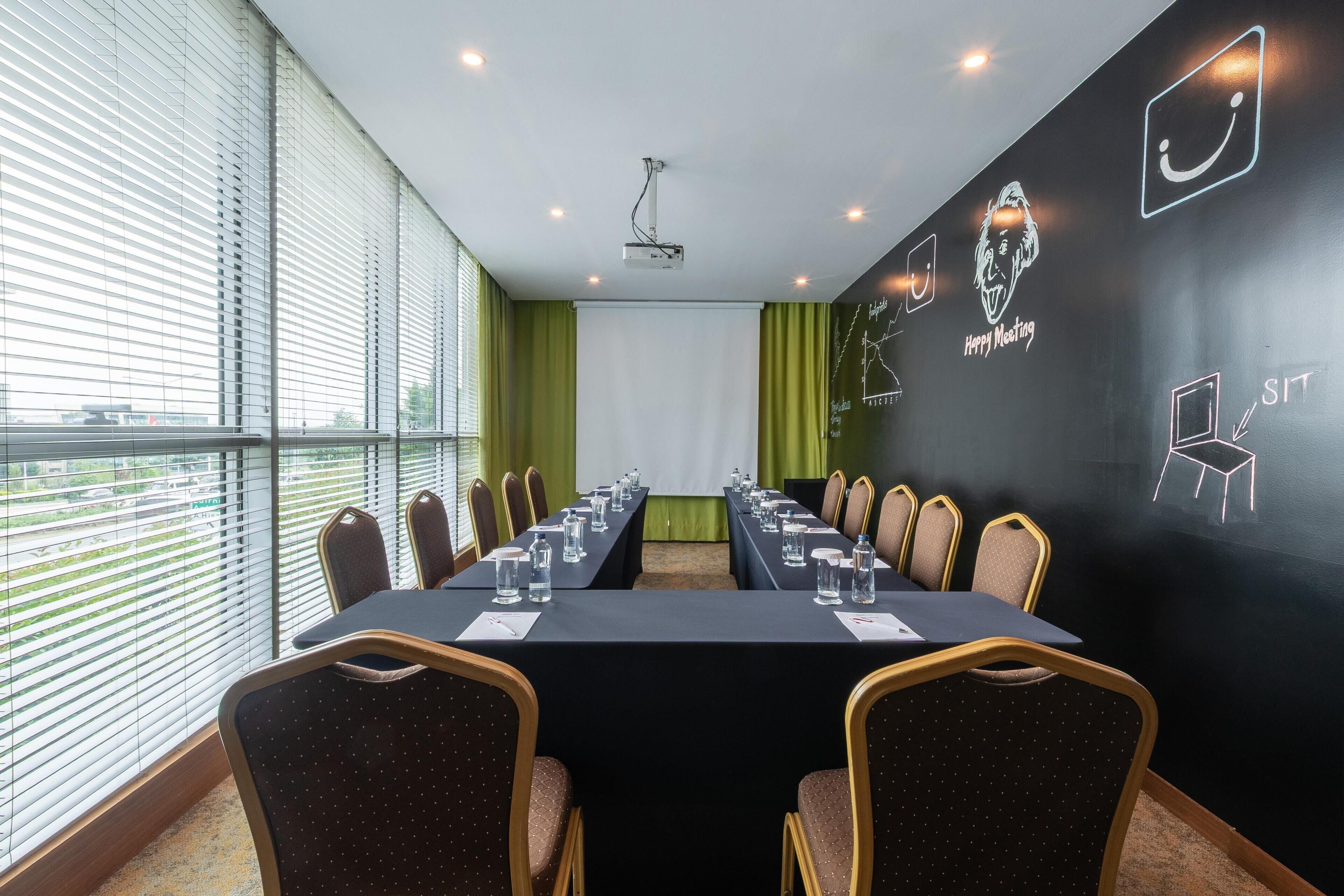 Ein Konferenzraum mit langem Tisch, Stühlen, einem Projektor und einer Wand mit Kreideanschriften.
