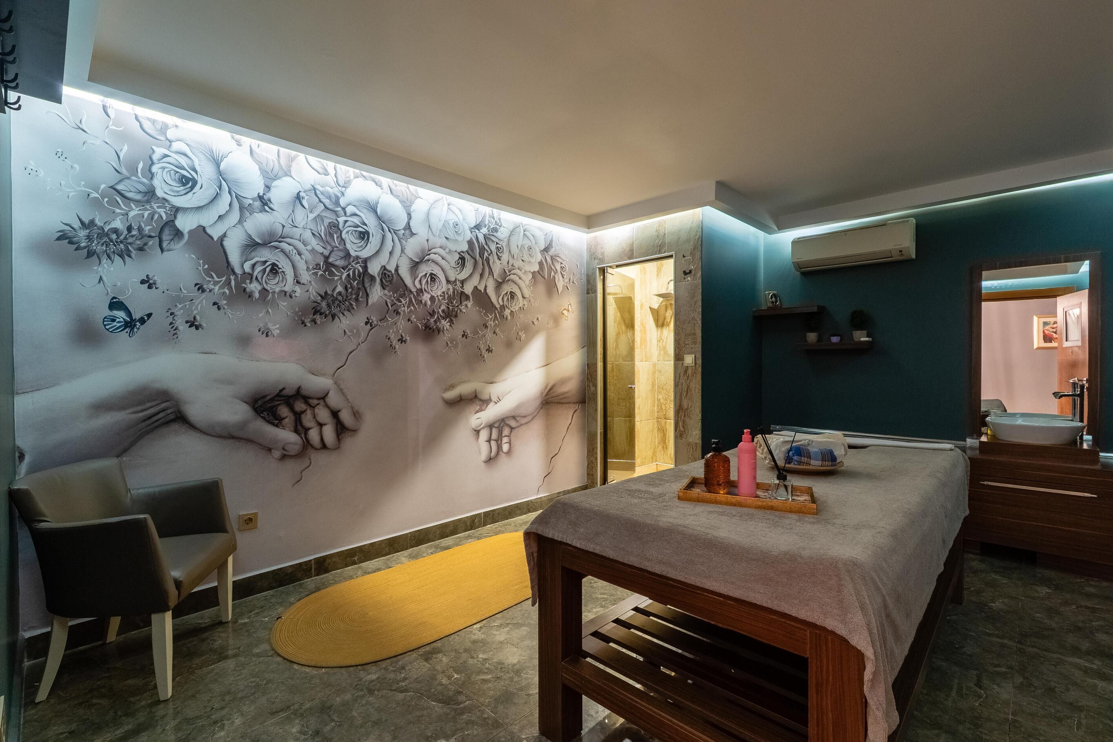 Una habitación con una mesa de masaje, una silla, un mural floral en la pared y un área de ducha.