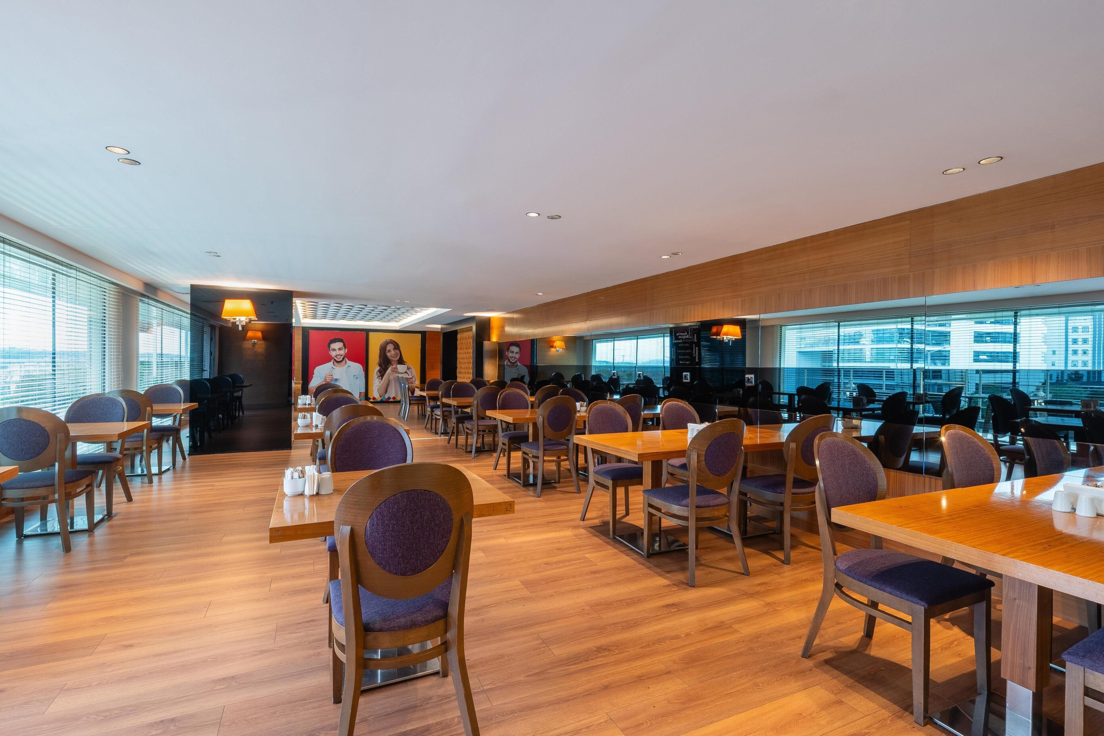 A modern dining area with wooden tables and chairs, large windows, and a city view.