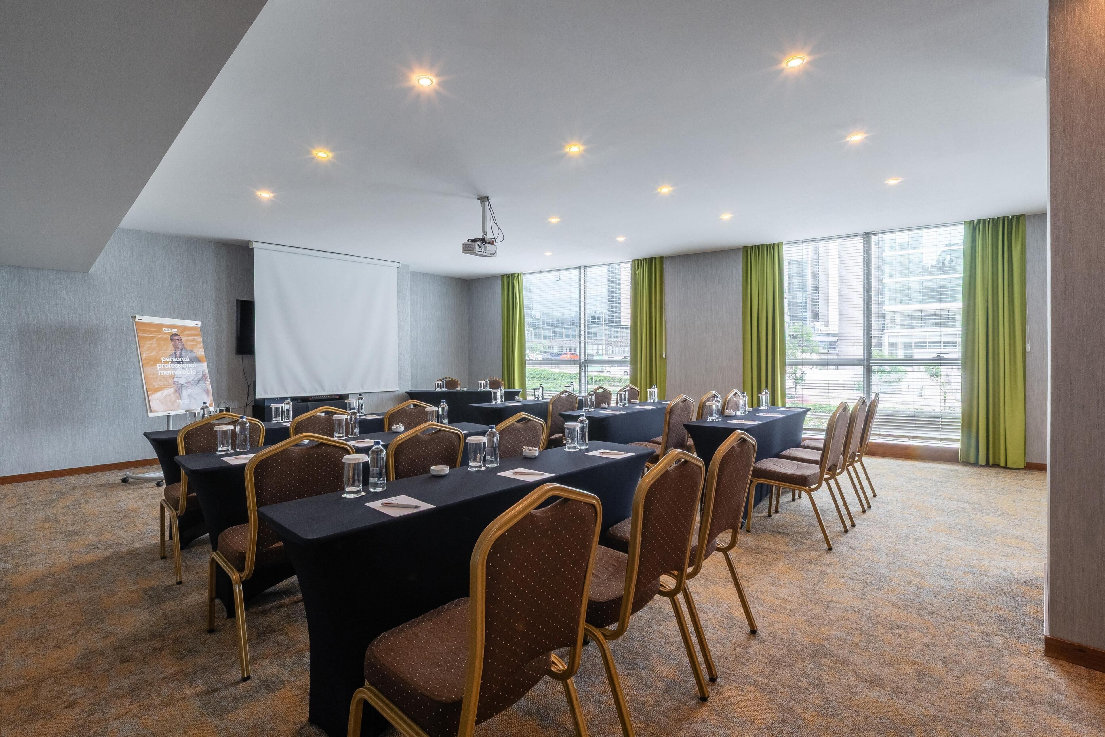 A conference room with tables and chairs, a projector, and a screen.