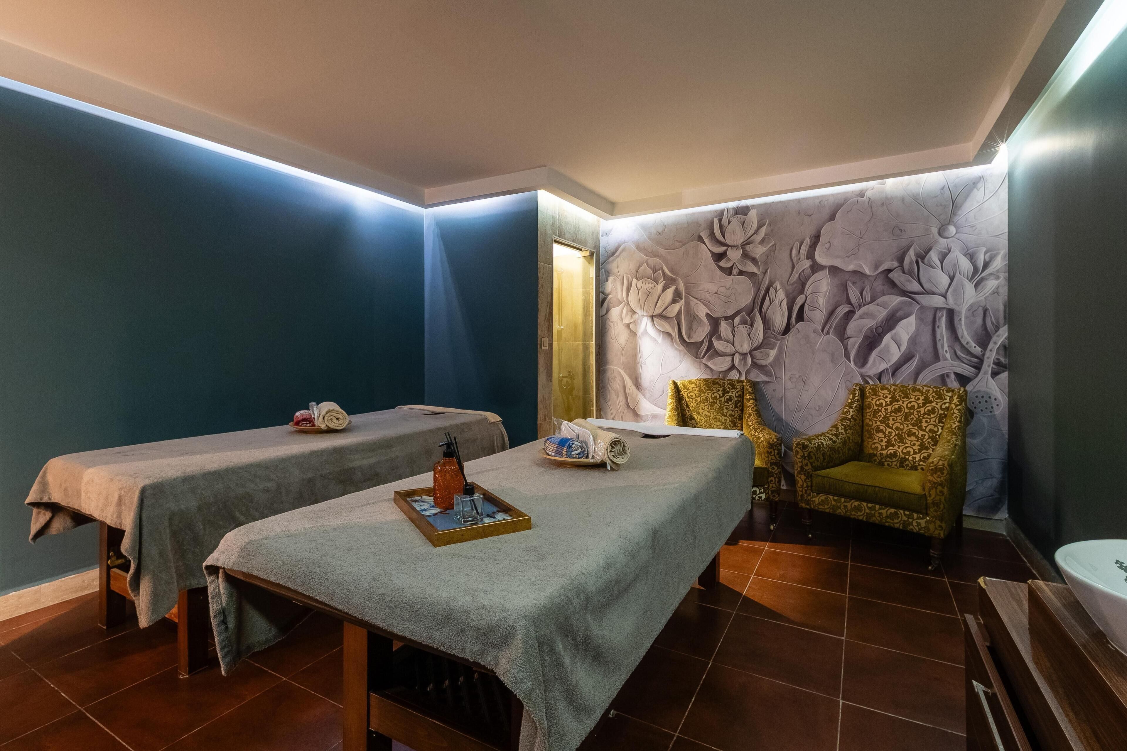 Un cuarto de spa con dos camillas de masaje, una silla y una pared decorativa.
