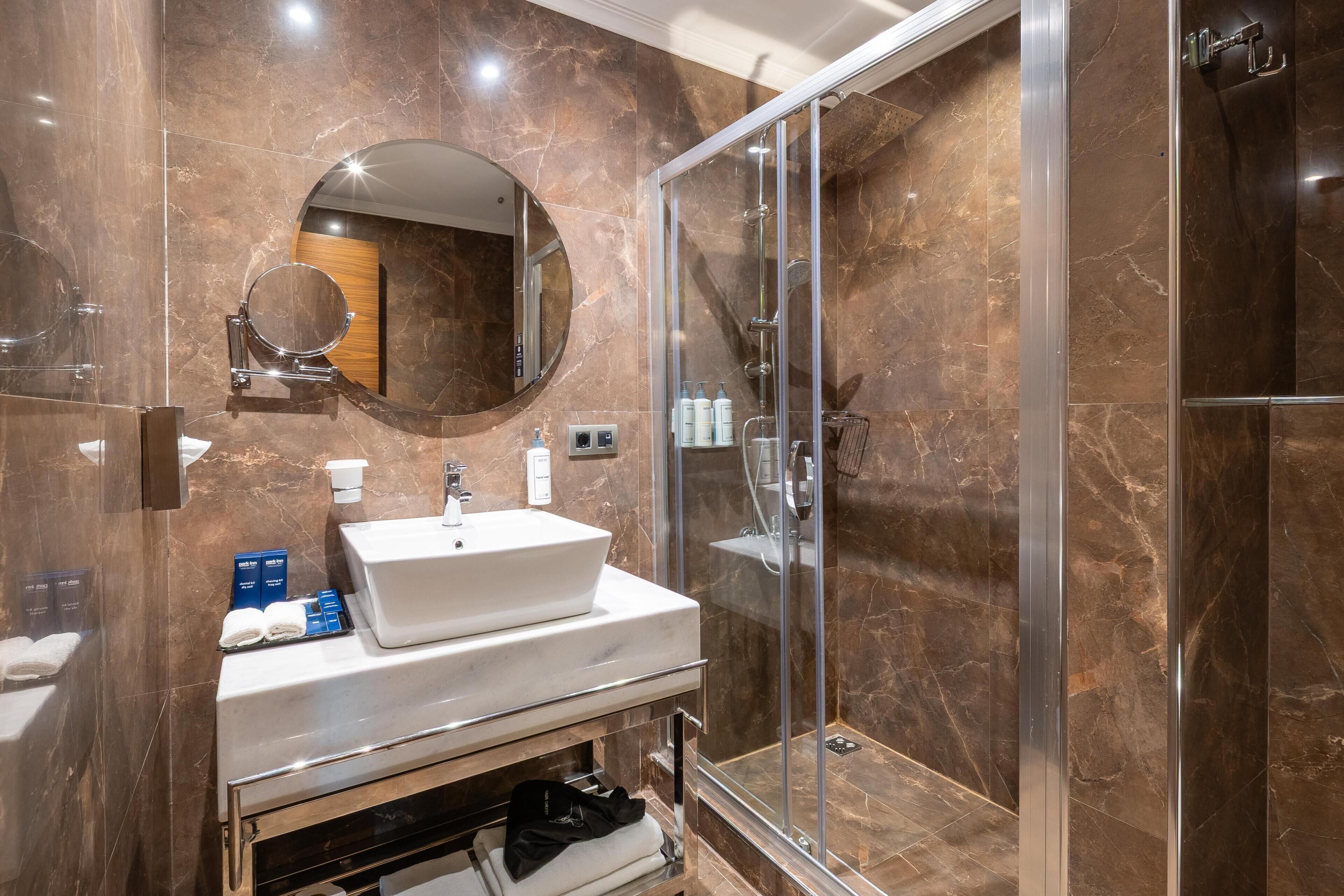 Een moderne badkamer met een marmeren wand, een wastafel, een spiegel en een glazen douchecabine.