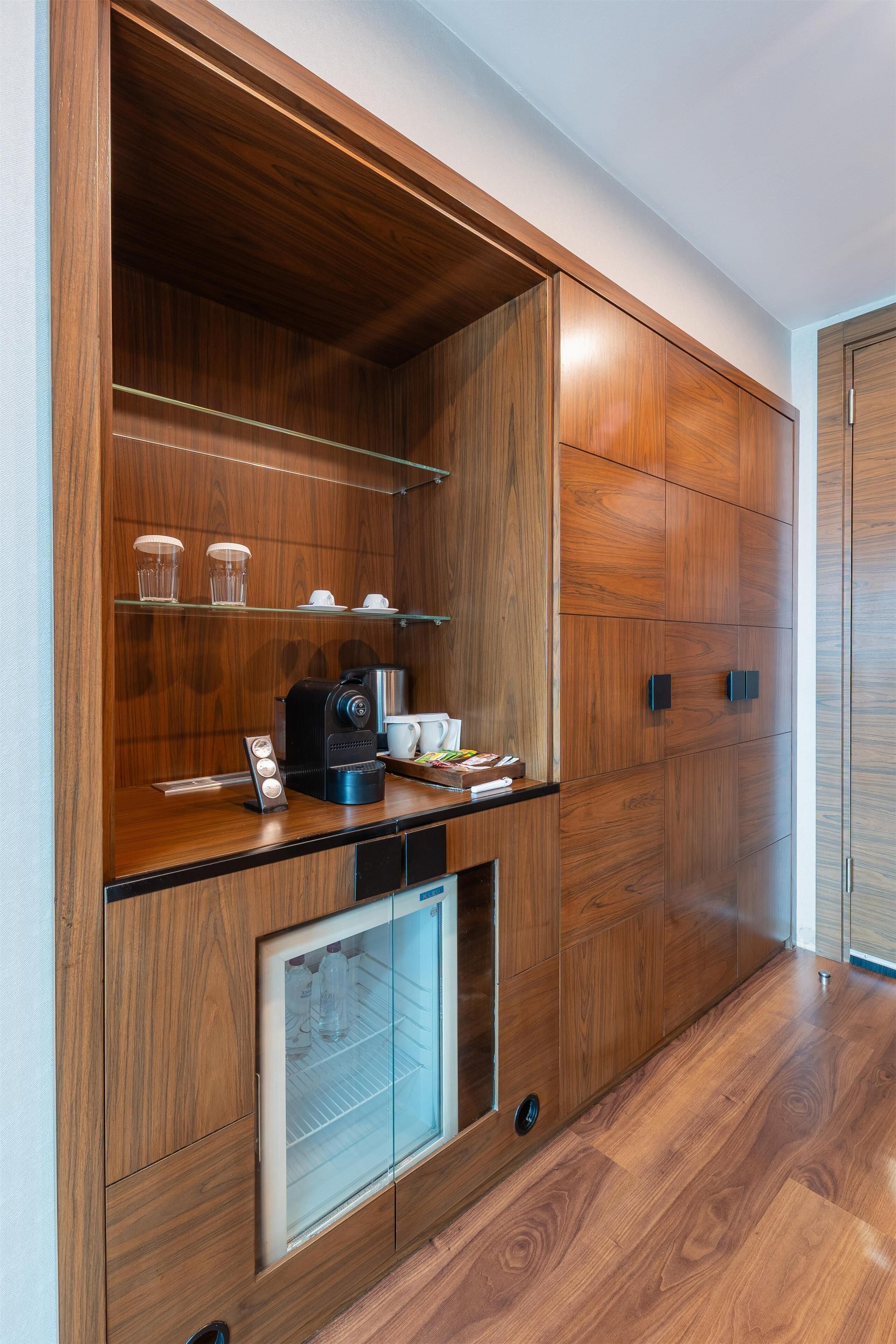 A modern kitchen with wooden cabinetry, a built-in coffee machine, and a mini-fridge.