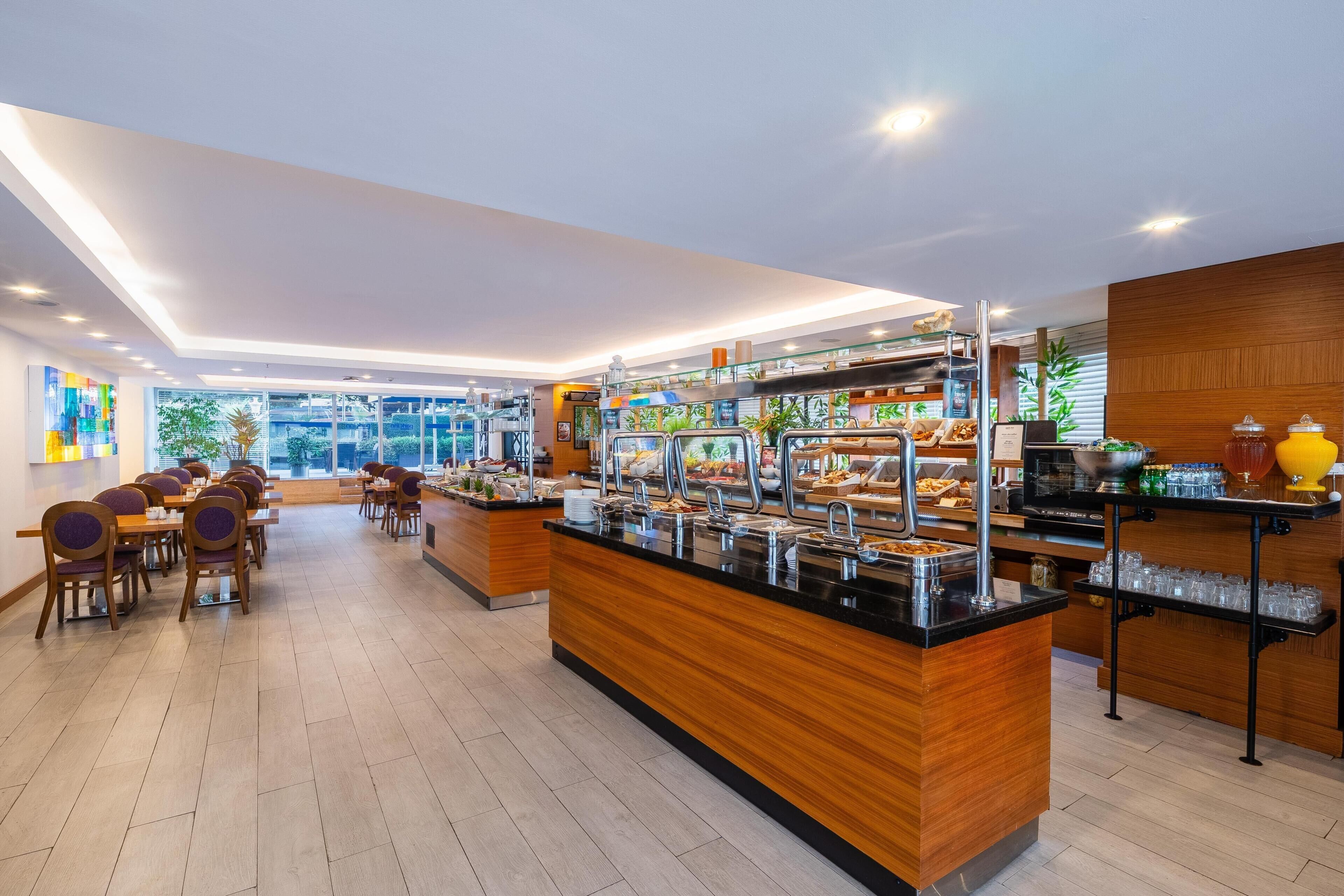 A modern breakfast area with a buffet setup, seating arrangements, and a view of the outdoors.