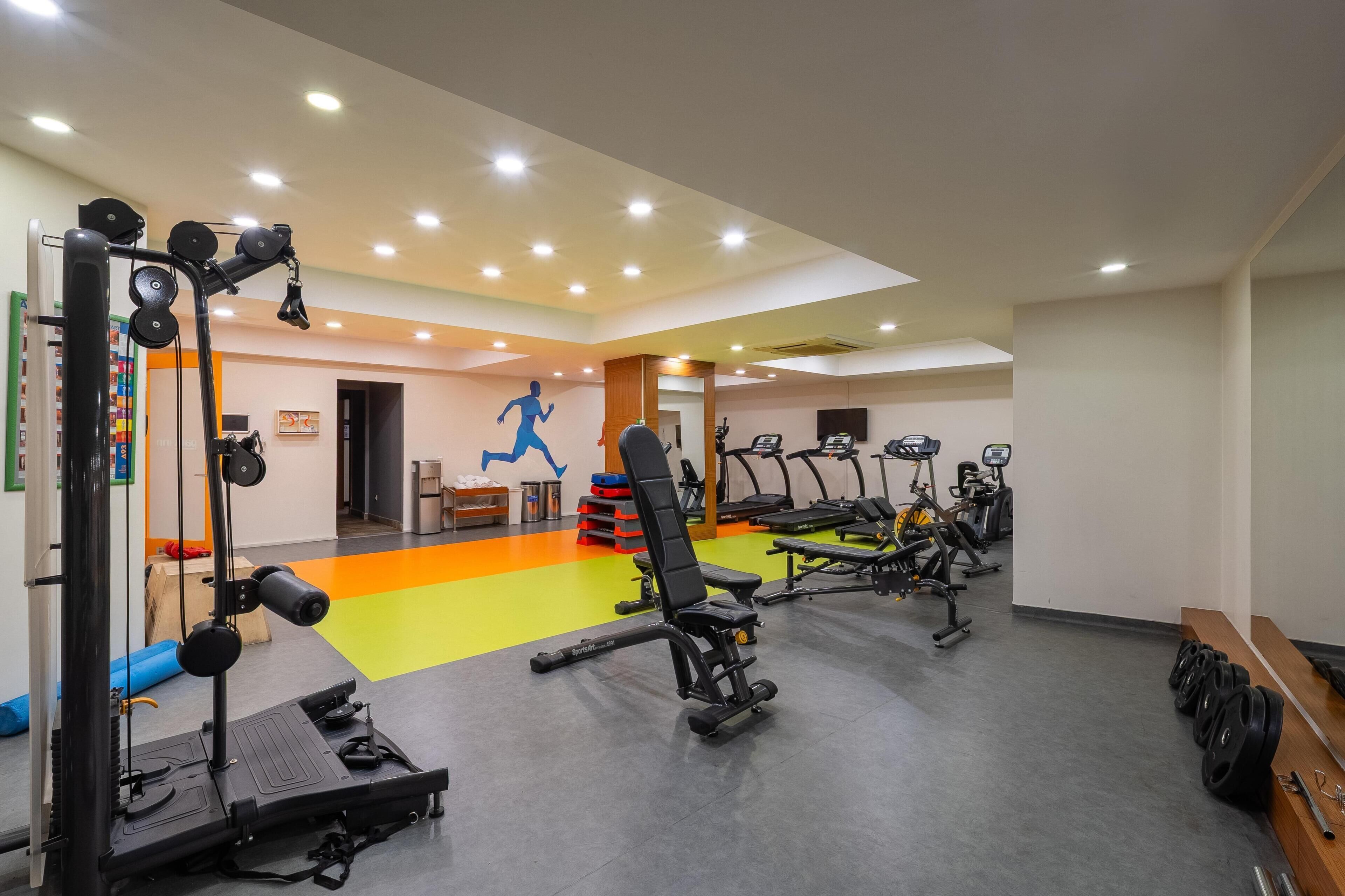 Une salle de sport équipée de divers appareils d’exercice, notamment des tapis de course, des appareils de musculation et un support à squats.