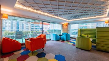 Un área de descanso moderna con alfombra hexagonal de colores, mobiliario contemporáneo y grandes ventanales con vistas a la ciudad.