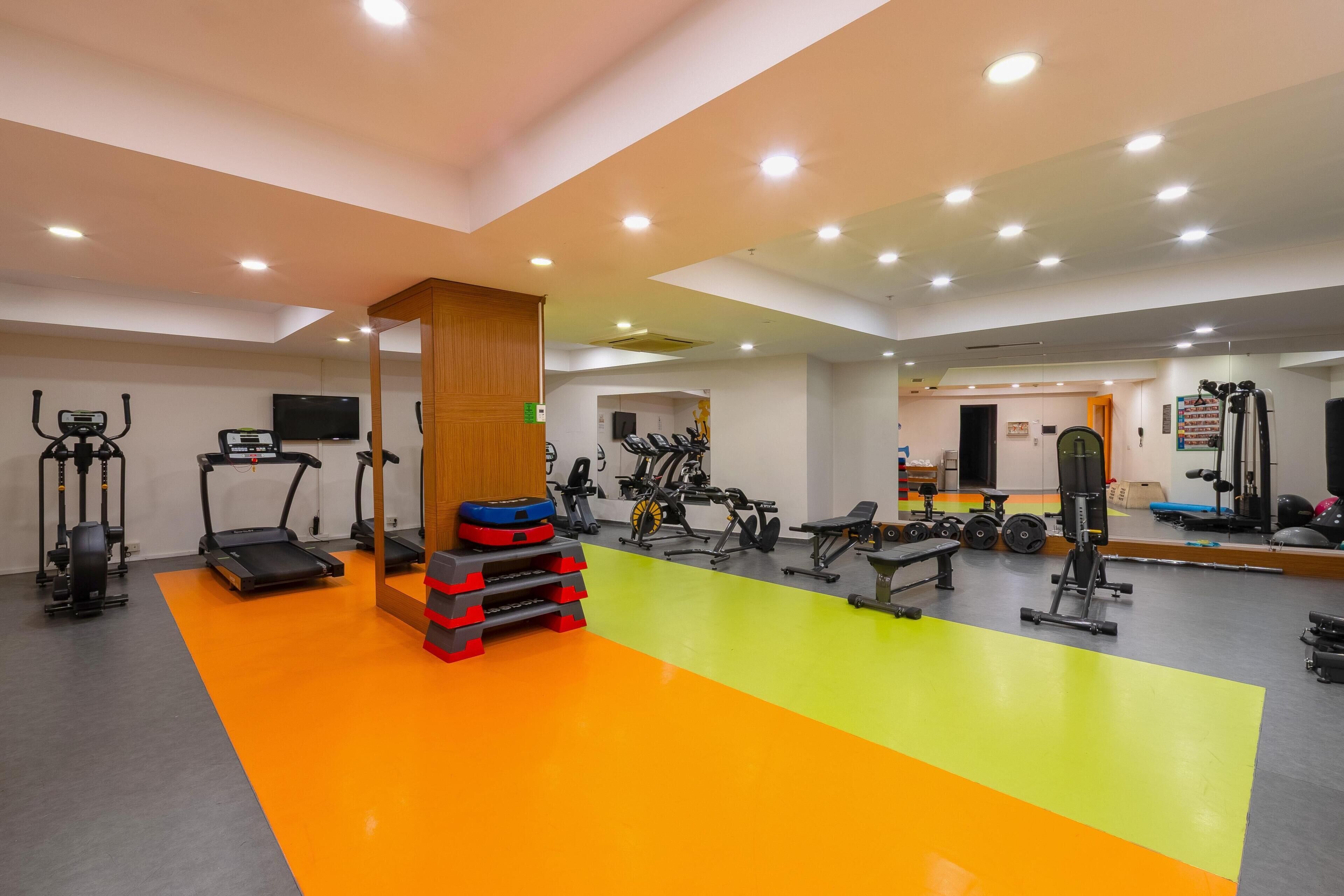 Un gimnasio interior bien iluminado con varios equipos de ejercicio, incluyendo cintas de correr, bicicletas estáticas y máquinas de pesas.