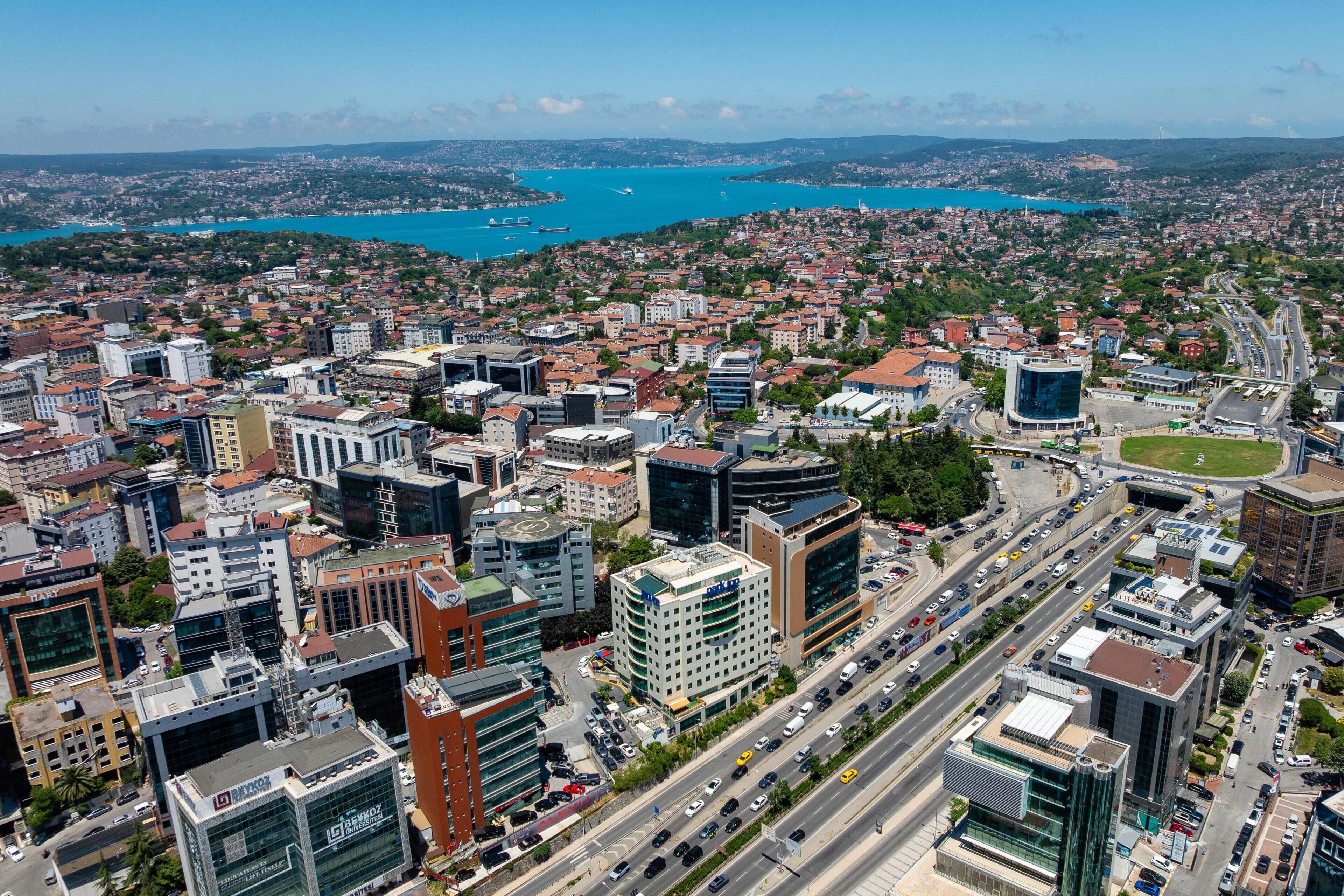 A cityscape with a mix of modern and traditional buildings, a busy road, and a large body of water in the background.