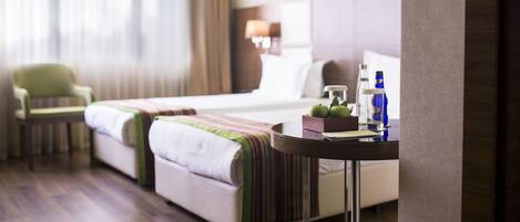 A hotel room with a bed, a chair, a table with a bottle, and a lamp.