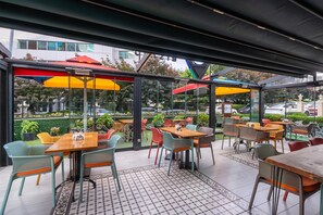 An outdoor café with tables and chairs, covered by umbrellas, and a view of the street and greenery. - Park Inn by Radisson Istanbul Asia Kavacik (Beykoz)