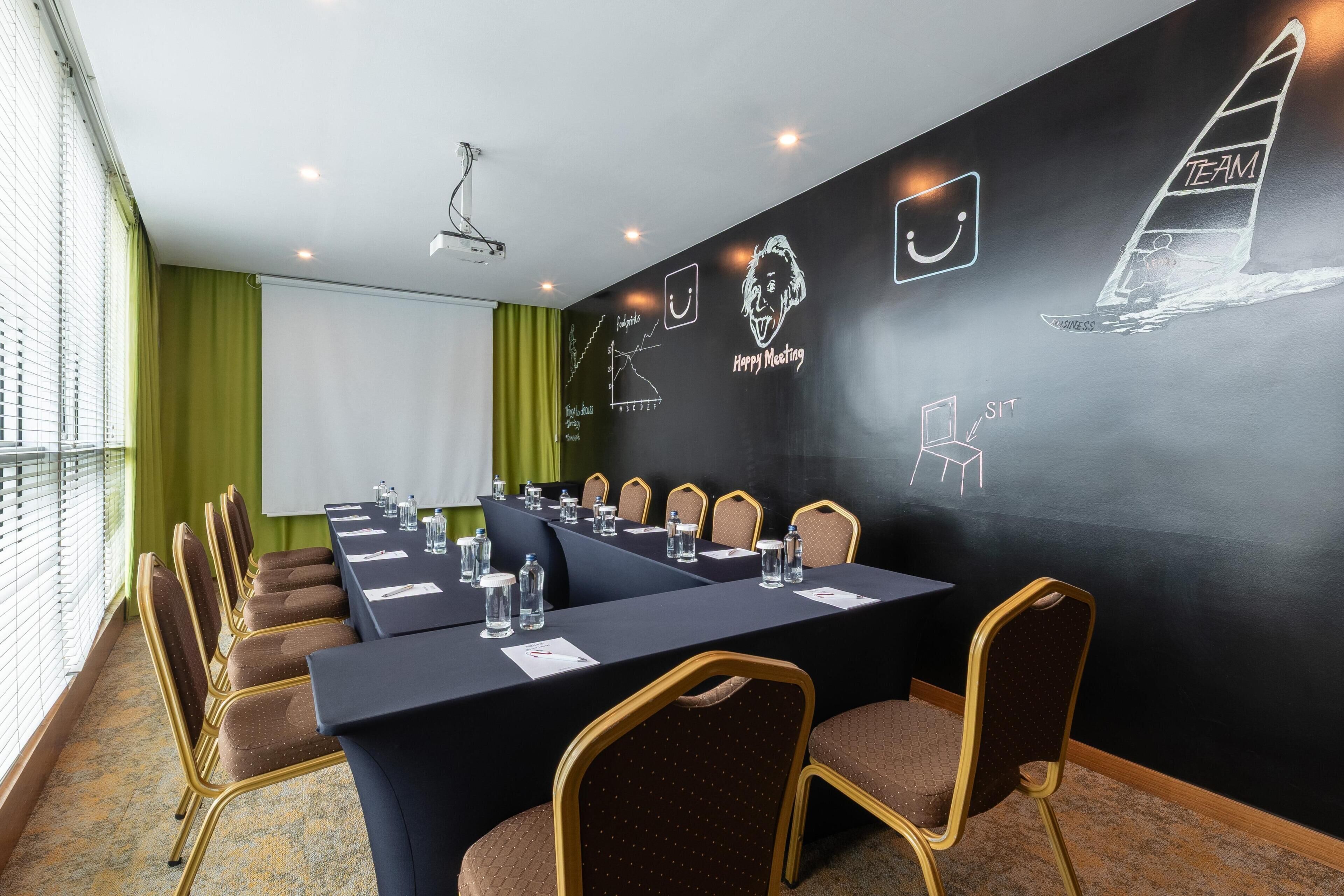 Una sala de conferencias con una larga mesa, sillas, una pantalla de proyector y una pizarra con diagramas relacionados con el mundo empresarial.