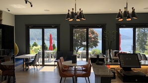 A modern dining area with a view of a lake, featuring a table with chairs, a computer, and a cash register. - Kokanee Glacier Resort (Nelson)