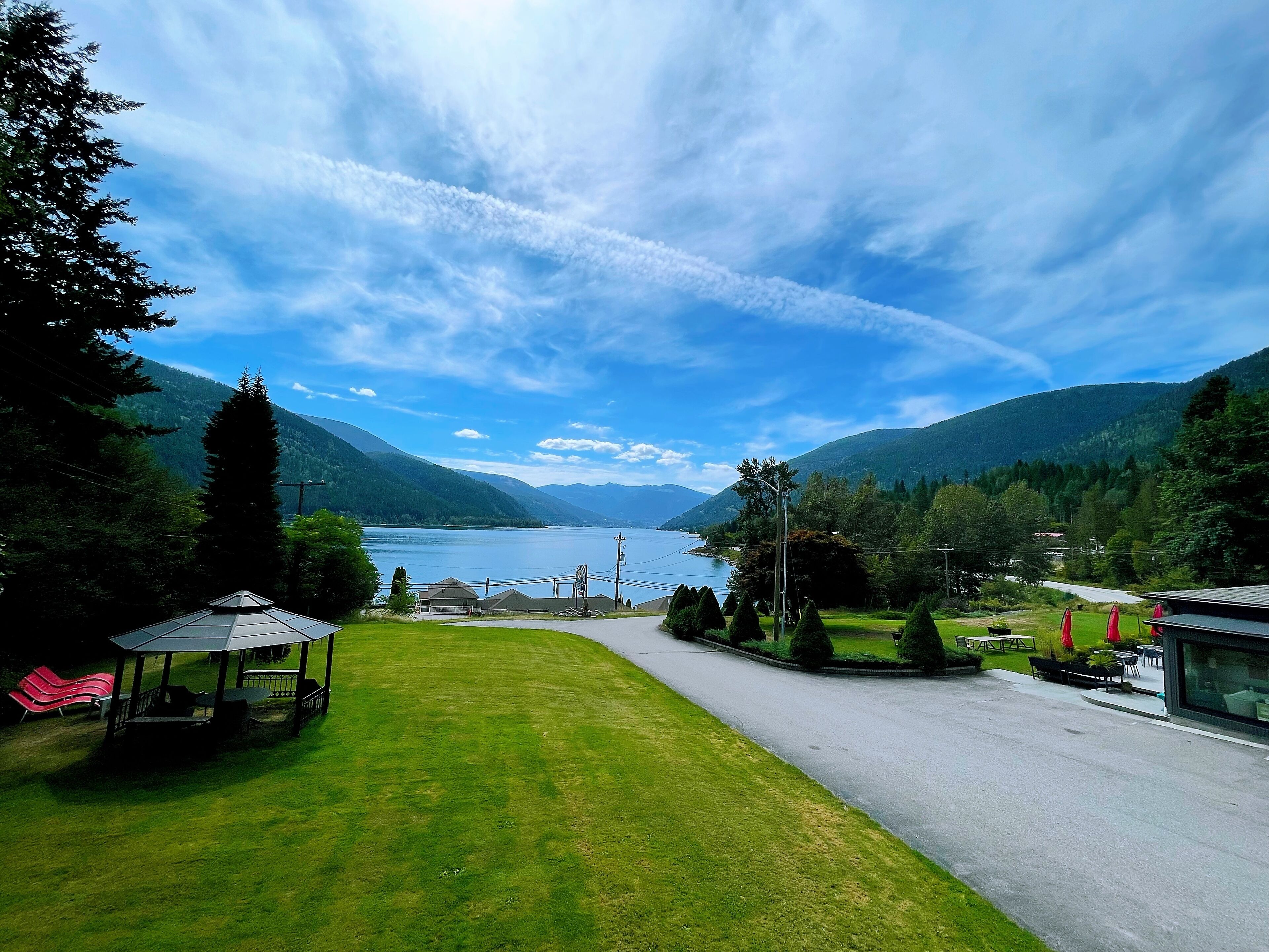 A lakeside view with a gazebo, a paved path, and a building with outdoor seating.